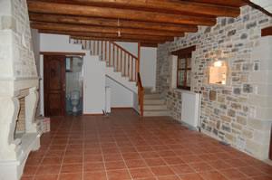 Wide angle picture showing living area, fireplace (left side), beamed roof and leading to lower bathroom. Stairs to upper floor.